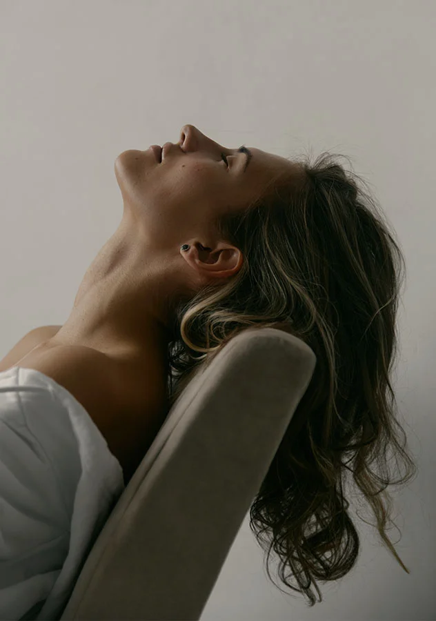 Side profile of a woman reclining in a chair, tilting her head back - Chin Augmentation in Grand Rapids, MI