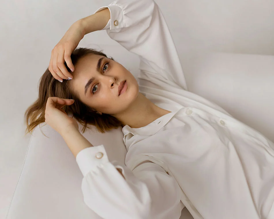 A woman in a white blouse, lying back and resting her hand on her forehead, with a serene and thoughtful expression - Clear and Brilliant Treatment in Grand Rapids, MI