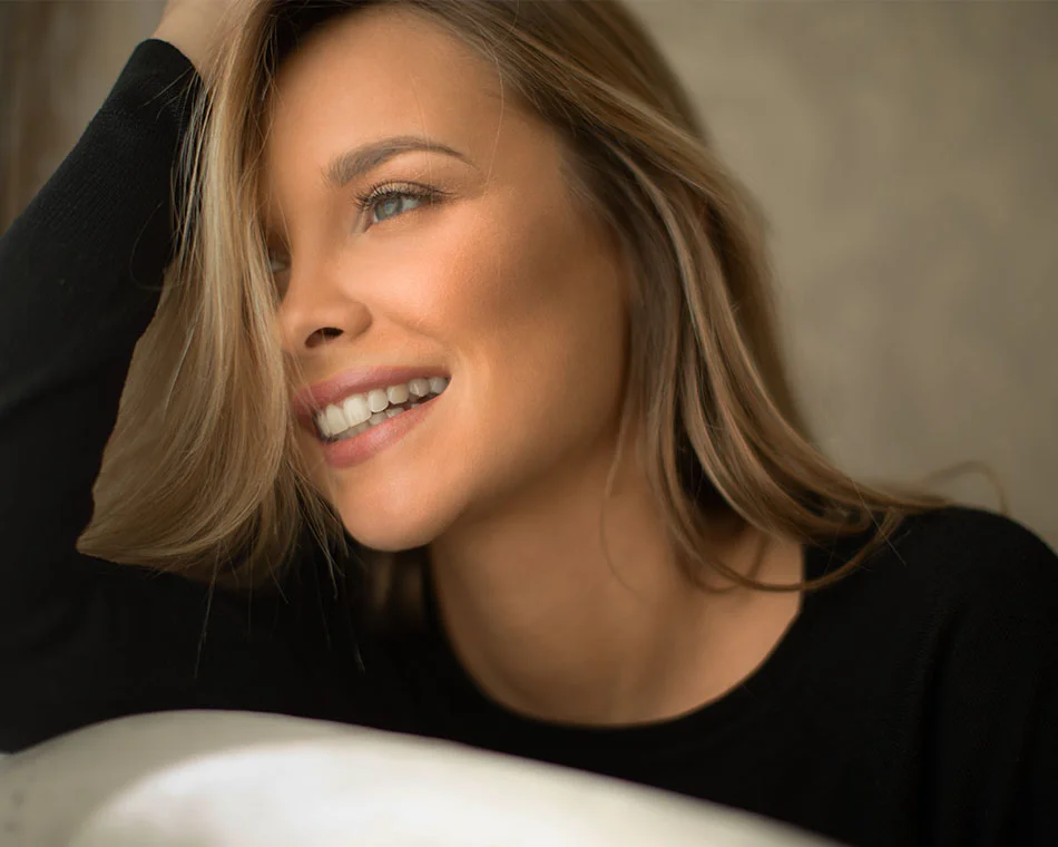 Smiling woman with light brown hair, resting her head on her hand, looking off to the side - Eyelid Surgery in Grand Rapids, MI