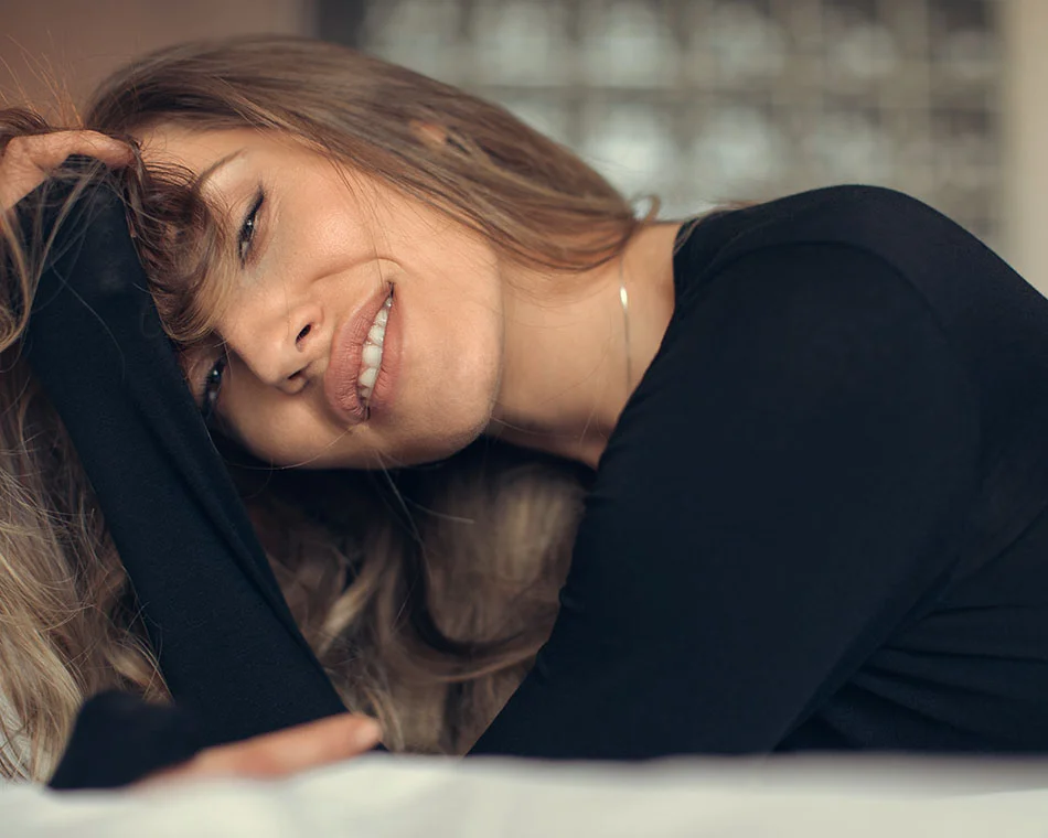 Smiling woman lying down with her hand resting on her head, dressed in a black top - Facial Implants in Grand Rapids, MI