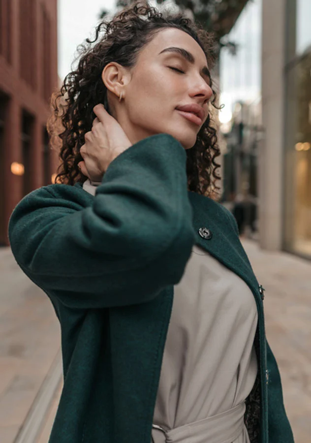 Curly-haired woman outdoors, eyes closed, enjoying the moment while gently holding her neck - Hydrafacial in Grand Rapids, MI