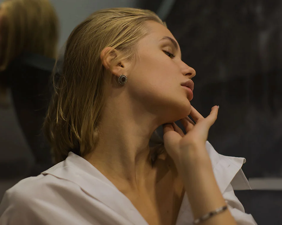 Woman with slicked-back blonde hair, tilting her head back and gently touching her neck, with a serene expression in a dimly lit room - Sciton BBL Laser in Grand Rapids, MI